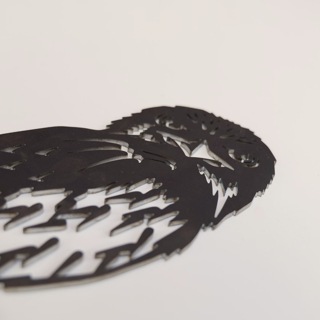 A close-up of Metalbird Australia's Tawny Frogmouth, a premium black metal silhouette, lies flat on a plain white surface, showcasing intricate cutout details for the eyes, beak, and feathers.