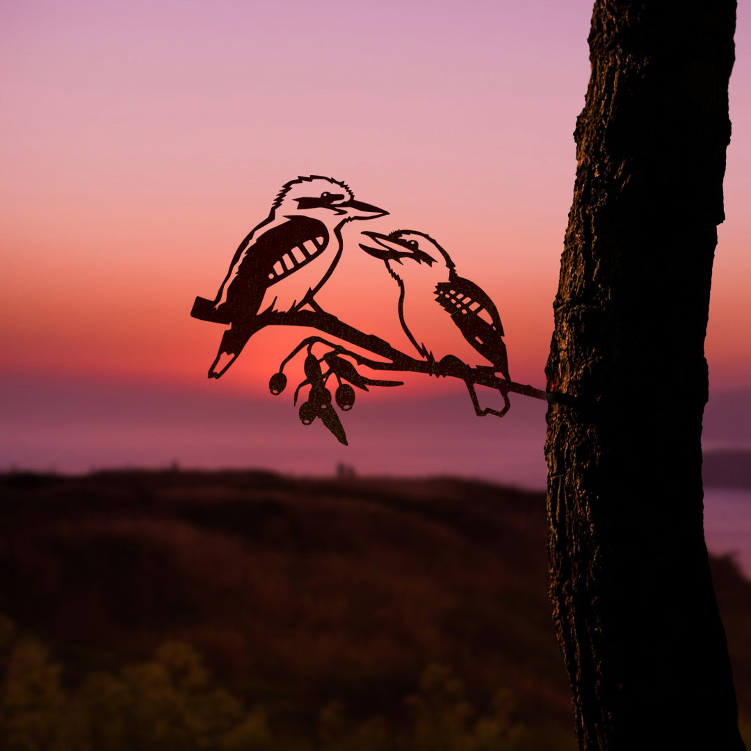 Pair of Kookaburras by Metalbird Australia—two kookaburras perched on a branch, crafted in corten steel, silhouetted against a sunset sky. A unique piece of yard art or thoughtful gift for bird lovers.