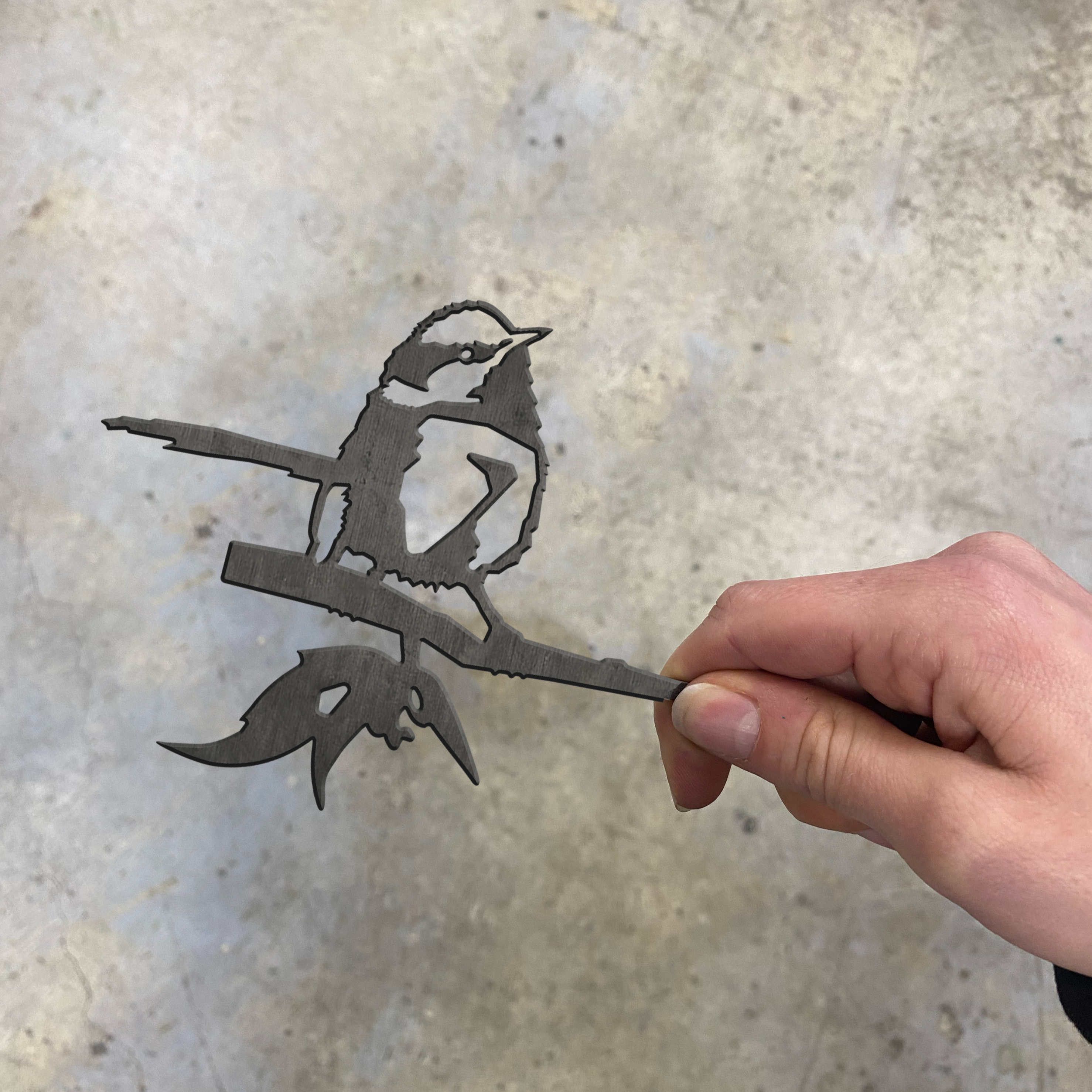 A hand holds the Metalbird Australia Blue Wren Mum & Mini Set, a unique metal bird silhouette perfect for yard art, shown against a gray mottled background.