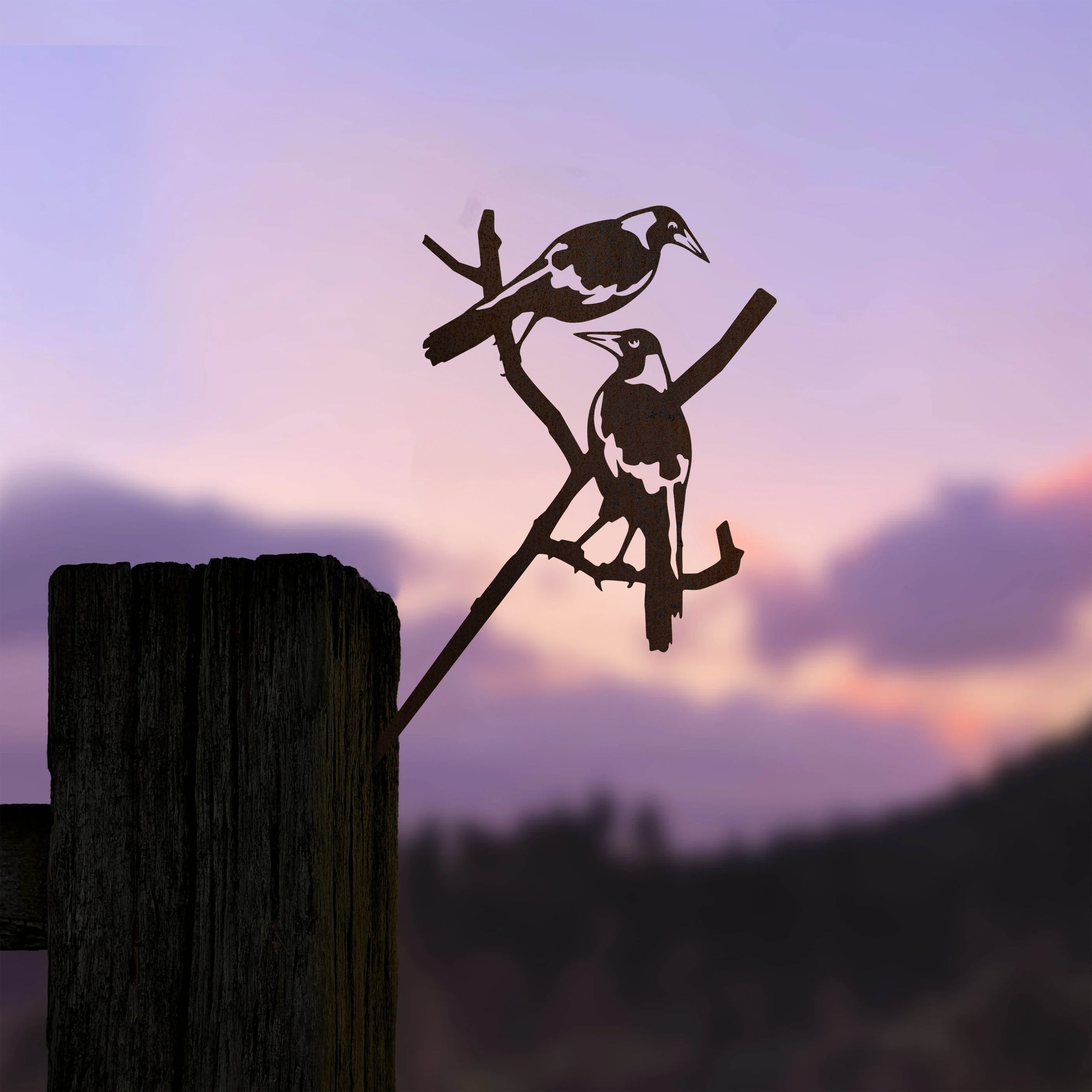 Pair of Magpies by Metalbird Australia—two magpies perched on a branch, crafted from metal and mounted on a post, silhouetted against a sunset sky. A perfect gift for nature lovers.