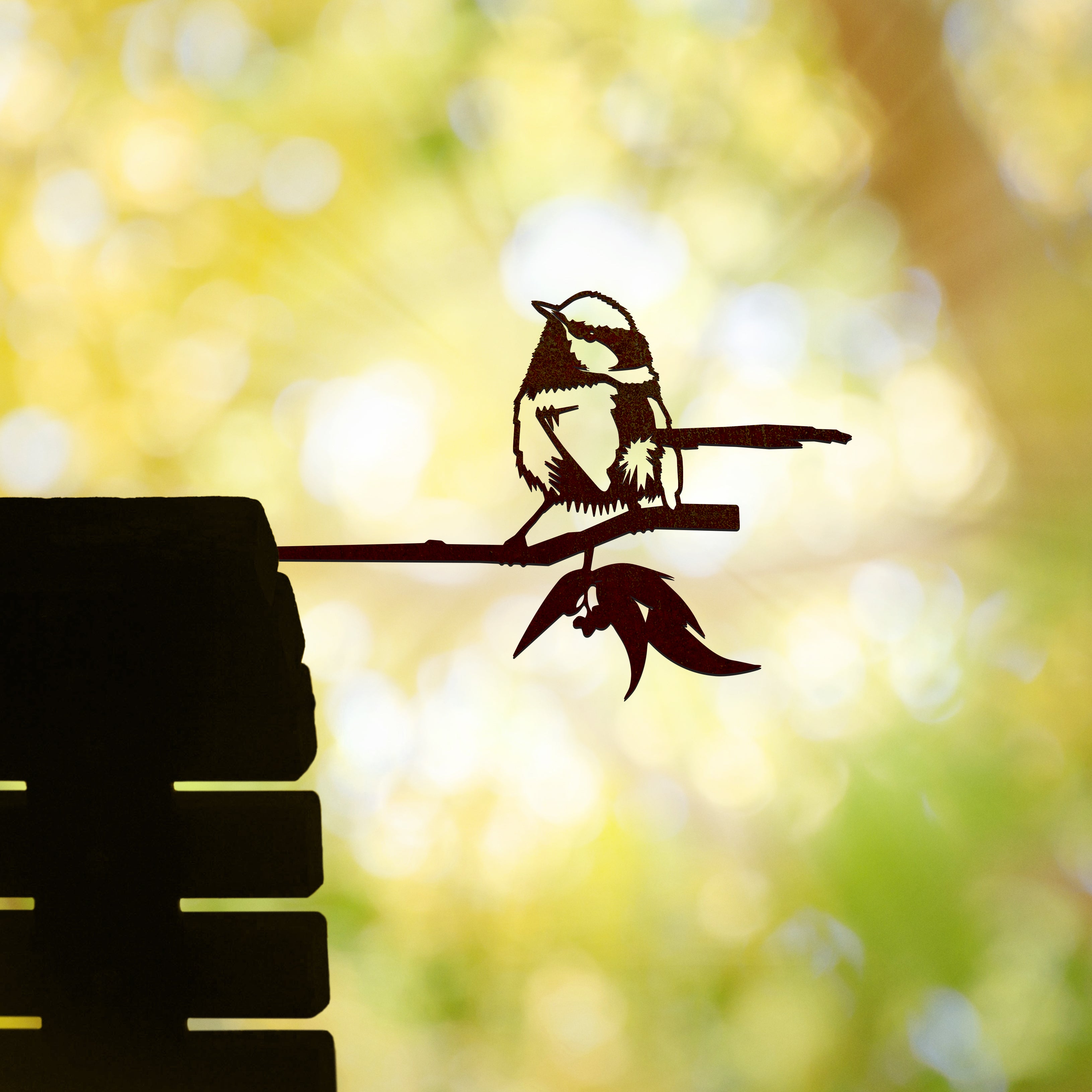 The Blue Wren by Metalbird Australia is a corten steel silhouette of a bird perched on a branch, set against a sunlit yellow-green background—sunbeams through trees create a peaceful scene, making it an ideal gift for nature lovers.