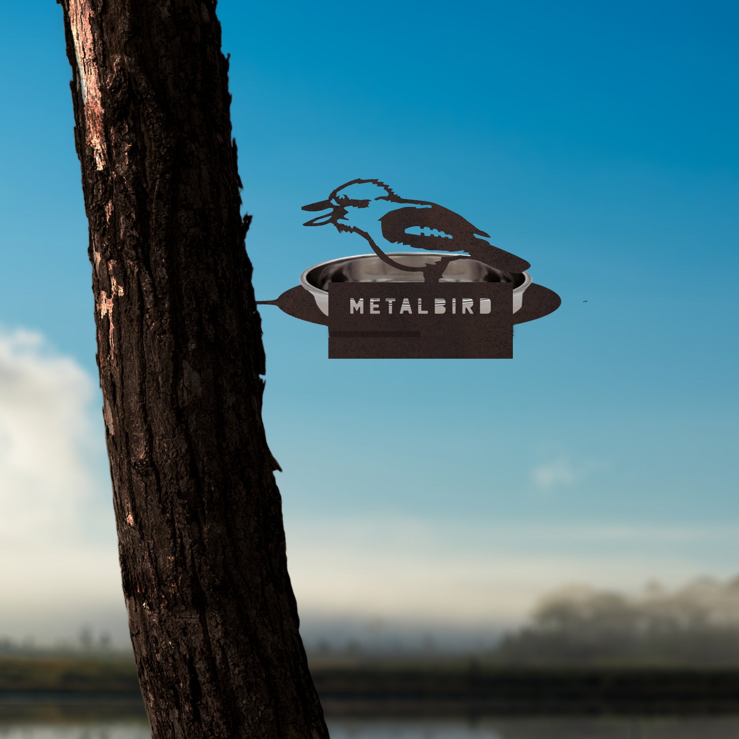 A Water Bowl Feeder by Metalbird Australia is attached to a tree trunk, offering eye-catching yard art against a clear sky and blurred landscape—an ideal gift for nature lovers.