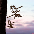 The Metalbird Australia Blue Wren Mum & Mini Set features two premium metal bird silhouettes on branches, attached to a tree trunk—an elegant yard art addition perfect against a pastel sunrise or sunset sky.