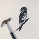 A Metalbird Australia "Tawny Frogmouth" metal bird cutout is displayed on a white surface beside a premium metal hammer with a black handle.