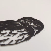 A close-up of Metalbird Australia's Tawny Frogmouth, a premium black metal silhouette, lies flat on a plain white surface, showcasing intricate cutout details for the eyes, beak, and feathers.
