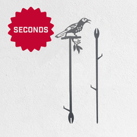 Illustration features Metalbird Australia - Seconds' Metalbird Seconds: metal garden art of a bird on a branch, with two decorative stakes, shown on white. A red starburst labeled "SECONDS" marks these discounted items with minor imperfections.