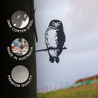 A striking piece of outdoor garden decor, the Southern Boobook Owl by Metalbird Australia is a metal silhouette crafted from 3mm Corten Steel and perched on a branch attached to a tree. Three circles highlight its features: Made in Australia, Premium Quality, and durable 3mm Corten Steel. With the fence and sky visible in the background, this premium Metalbird sculpture adds charm to any natural setting.