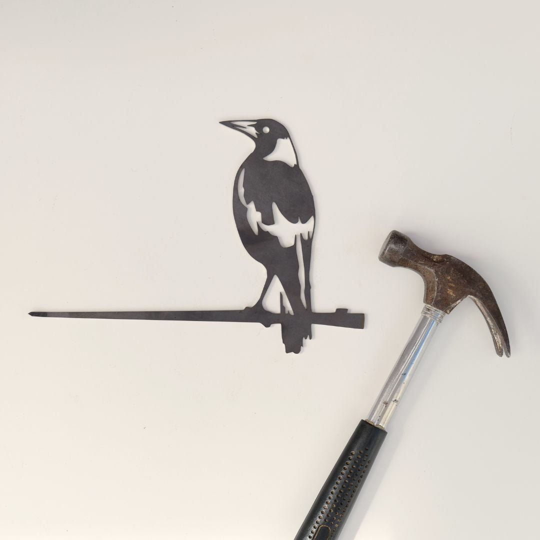 Magpie steel silhouette and a wooden-handled hammer on a pale background.