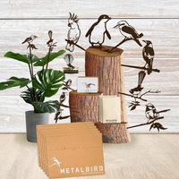 A display of Metalbird Australia’s Christmas Signature Gift Pack: Corten steel bird silhouettes on wooden blocks, a potted plant, and branded envelopes, set against a light wood background—an ideal festive gift.