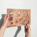 Two hands hold a rectangular metal sheet featuring five decorative bird cutouts from the Winged Hangers - 5 Festive Decorations by Metalbird Australia. The sheet casts bird-shaped shadows on a white background.