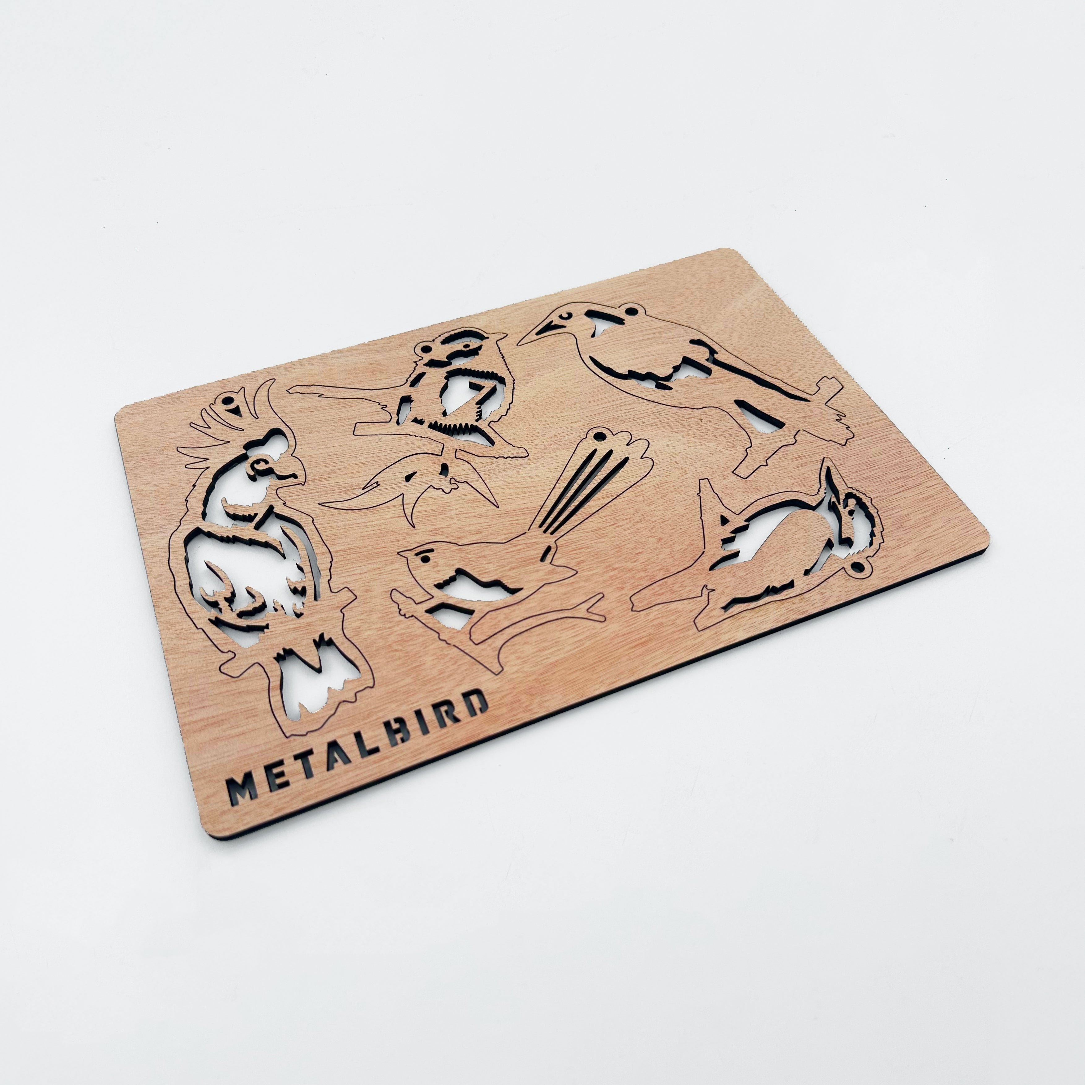 A thin wooden sheet from sustainably grown wood features cut-out silhouettes of festive birds labeled "Winged Hangers - 5 Festive Decorations" by Metalbird Australia, displayed on a plain white background.