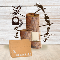 Three stacked wooden logs feature black metal birds from Metalbird Australia. In front, brown branded envelopes and a wrapped package sit against a light wood backdrop—a perfect Christmas Favourites Gift Pack.