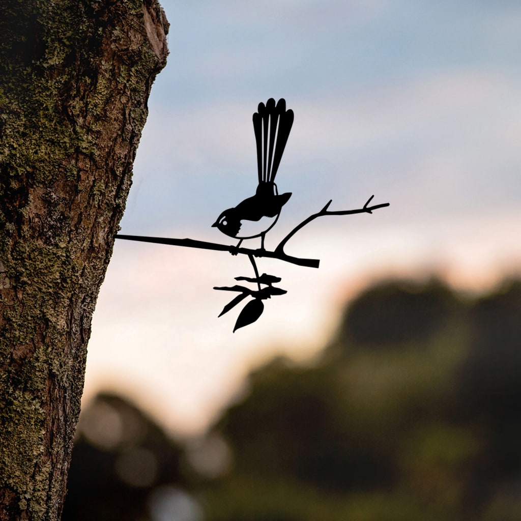 Willie Wagtail silhouette mounted on a tree with an evening garden behind.